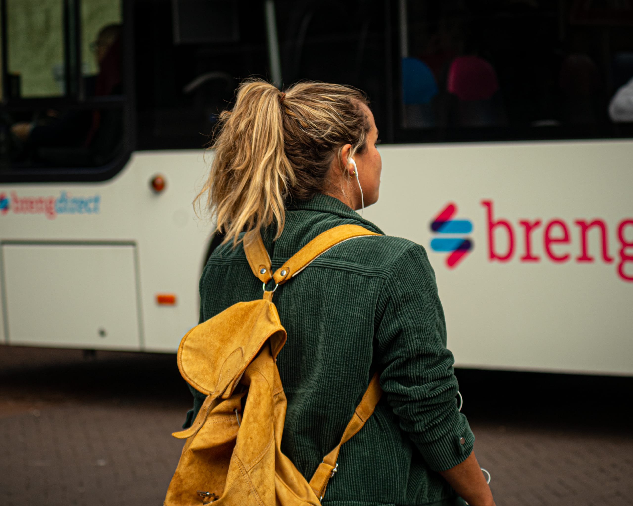 Street photograph: a woman with a yellow backpack beside a bus