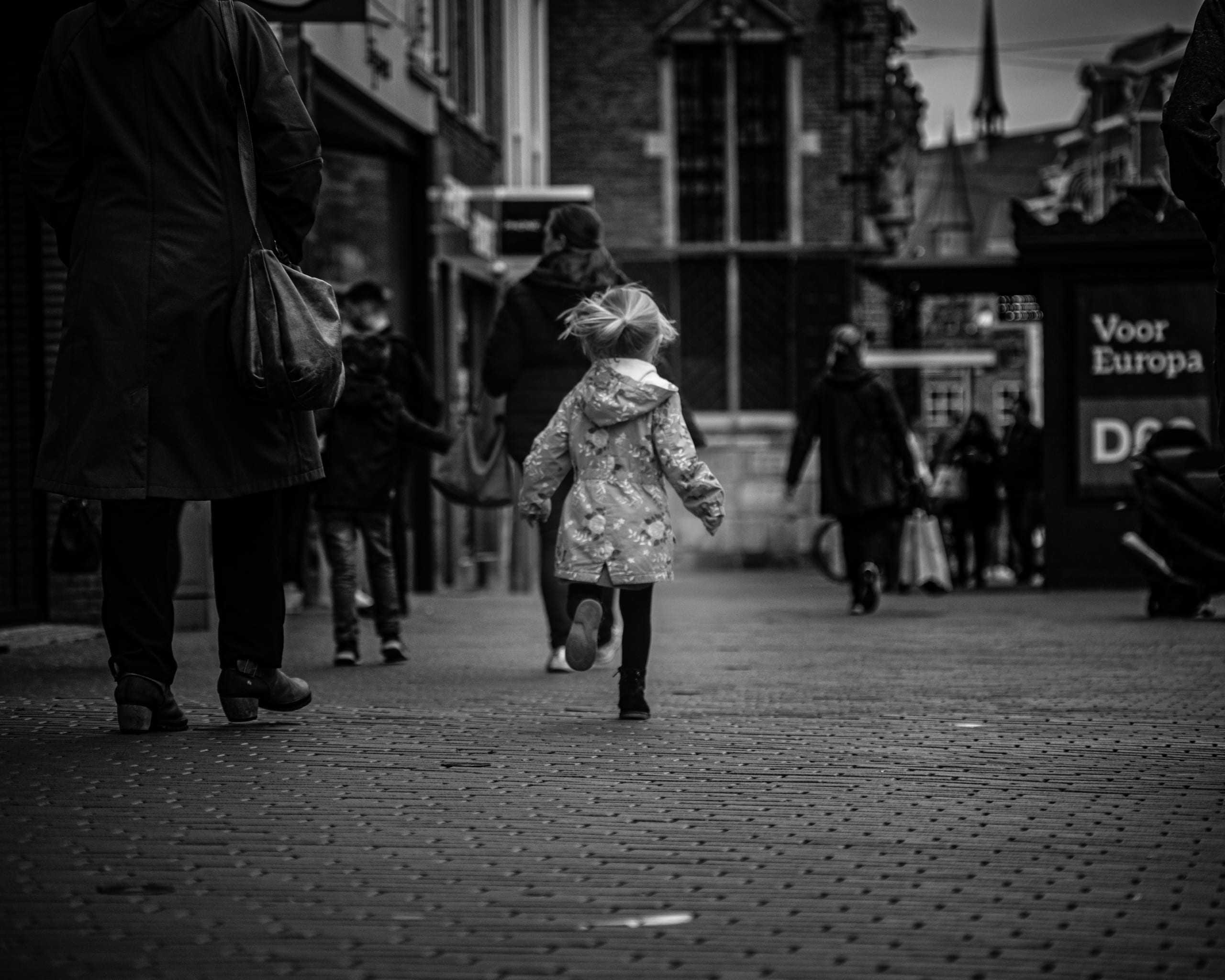 Black-and-white street photograph: a child running through a crowd